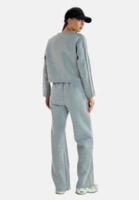 Felpa grigia corta e pantaloni abbinati realizzati in materiale morbido. L'outfit presenta una vestibilità rilassata ed è abbinato a un cappellino nero.