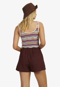 Mønstret tanktop i flere farver med rund halsudskæring, parret med maroon linnedshorts. Modellen bærer en brun bucket hat. Vist fra ryggen.