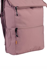 Sac à dos en tissu rose avec un dessus zippé, une poche avant et une poche en maille sur le côté. Comprend un détail de logo et une surface lisse et texturée.