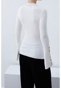 Biały, prążkowany top z długim rękawem, z wysokim kołnierzem ozdobionym perełkami z tyłu oraz guzikami na rękawach. W komplecie czarne spodnie.