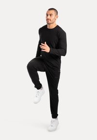 Czarna bluzka z długim rękawem i dresowe spodnie, wykonane z miękkiego materiału, o dopasowanym kroju i elastycznych mankietach, w połączeniu z białymi sportowymi butami.