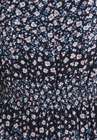 Kwiatowa sukienka z ciemnoniebieskim tłem i białymi oraz różowymi kwiatami. Ma plisowany fason i elastyczny pas dla lepszego dopasowania.