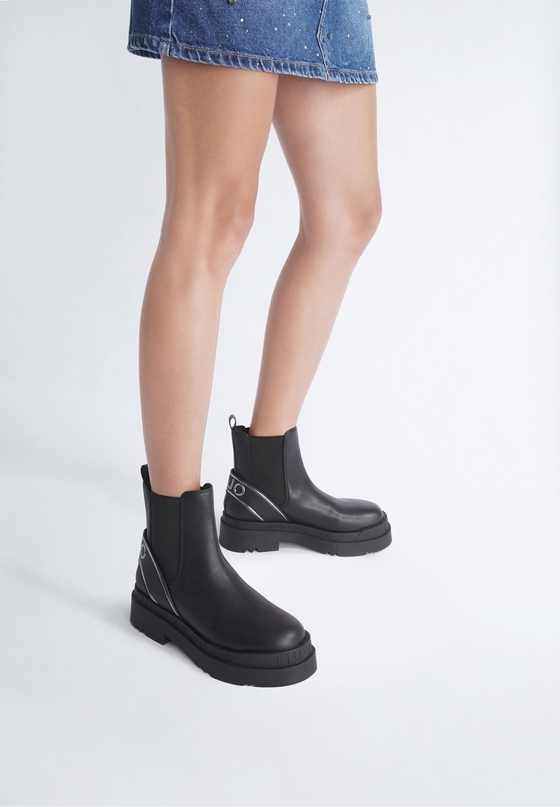 Schwarze Stiefeletten mit Gummisohle, elastischen Seitenpanelen und dekorativen silbernen Akzenten. Glatte Textur mit einem klobigen Absatzdesign.