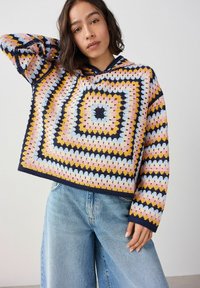 Sweter typu pullover na szydełku z kapturem, zdobiony kwadratowym wzorem w kolorach różowym, niebieskim, żółtym i granatowym. Wykonany z teksturowanej przędzy, o luźnym kroju.