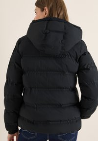 Doudoune noire avec capuche, dotée d'un design matelassé et d'une texture lisse. Coutures visibles le long des coutures et rembourrage gonflant.
