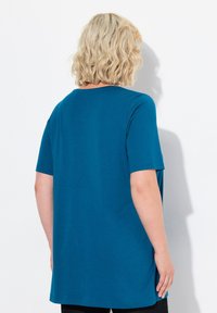 T-shirt oversize verde acqua con maniche corte, scollo rotondo e una texture liscia, abbinato a pantaloni neri.