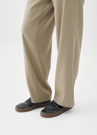 Sneakers nere con suole in gomma, cuciture bianche e finitura liscia, abbinate a pantaloni beige chiaro, larghi e comodi.