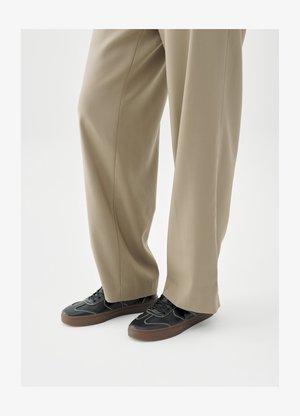 Fekete sportcipők gumi talppal, fehér varrással és sima felülettel, világos bézs, bő szabású nadrággal párosítva.