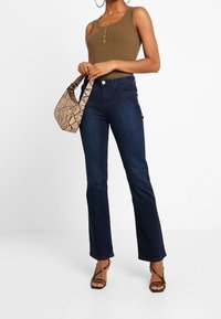 Ribbad olivgrön linne med knappar, mörkblå utsvängda jeans, handväska med ormskinnsmönster och svarta sandaler med remmar, vilket skapar en avslappnad outfit.