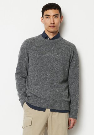 Grauer gestrickter Pullover mit Rundhalsausschnitt und gerippten Manschetten, über einem dunkelblauen Hemd mit Kragen getragen, kombiniert mit beigen Cordhosen.