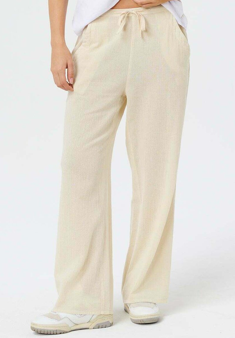 Pantalones de pierna ancha color beige claro hechos de tela suave, con cintura elástica con cordón y bolsillos laterales.