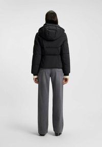 Svart vadderad pufferjacka med huva, med en figurnära överdel och lös underdel, i kombination med grå vida jeans.