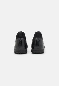 Schwarze Sportschuhe mit strukturierter Oberfläche, ausgestattet mit einer Schlaufe und gepolsterten Sohlen. Minimalistisches Design mit subtilen reflektierenden Akzenten.