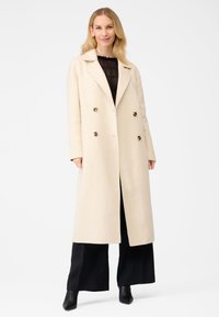 Beige uldblandings dobbeltbrystet frakke med spids krave, store brune knapper, lange ærmer og lige snit, med en slids bagpå.