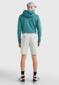 Felpa con cappuccio color teal, pantaloni corti chiari e sneakers multicolori. Le caratteristiche includono un cappuccio prominente e due tasche posteriori sui pantaloni corti.