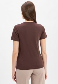 Korte mouwen bruine t-shirt met ronde hals van zachte stof, met een eenvoudig ontwerp. Van achteren weergegeven, in combinatie met lichtgekleurde broek.