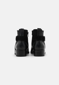 Botas de tobillo de cuero negro con un acabado texturizado, cremalleras laterales, paneles elásticos y un tacón bajo y cuadrado. Tacón reforzado y detalle de correa decorativa.