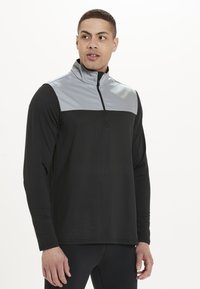 Sort langærmet pullover med et gråt panel over brystet, halvdels lynlås krave og glat stof. Har en afslappet pasform.