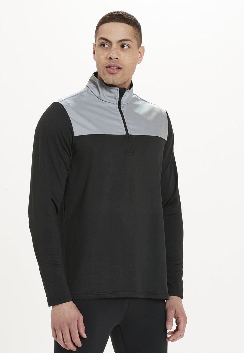Zwarte lange mouwen pullover met een grijze baan over de borst, halve ritssluiting kraag en een gladde stof. Heeft een ontspannen pasvorm.