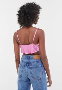 Růžový saténový crop top s tenkými ramínky, který je kombinován s modrými džíny s vysokým pasem a koženou nášivkou na zadním pásku.