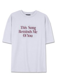 Lühikeste varrukatega, valge puuvillane T-särk, millel on burgundi värvi tekst: "See laul tuletab mind sinust meelde" julge serifikirjaga.