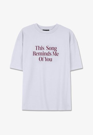 Lühikeste varrukatega, valge puuvillane T-särk, millel on burgundi värvi tekst: "See laul tuletab mind sinust meelde" julge serifikirjaga.