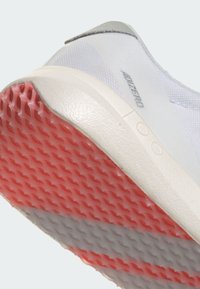 Chaussure de sport blanche avec une tige en maille texturée, des accents gris et une semelle en caoutchouc rose/gris présentant un motif en nid d'abeille.