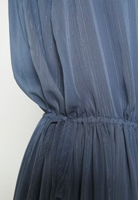 Robe bleu semi-transparente avec texture plissée, taille élastique et subtils accents de fil métallique à travers le tissu.