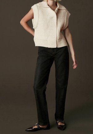 Gilet en tricot couleur crème avec texture côtelée, manches courtes et col à revers, associé à un jean noir droit et des ballerines pointues.