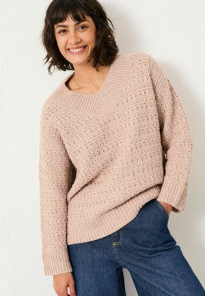 Light pink knitted sweater with a V-neck, textured pattern, and ribbed cuffs, paired with dark blue denim jeans.