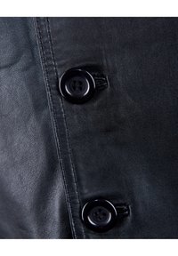 Schwarzes Ledergewebe mit einer glatten Textur, das eine sichtbare Naht und einen großen, glänzenden Knopf mit vier Löchern aufweist.
