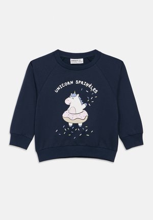 Tumesinine laste pusa, millel on multikaliselt ükssarvik, kes istub glasuuriga kaetud sõõrikus, ning tekst "UNICORN SPRINKLES" ülalt.