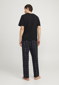Zwarte katoenen t-shirt in combinatie met marineblauwe geruite pyjamapantalons met witte en blauwe lijnen, die een ontspannen pasvorm en zachte textuur tonen.