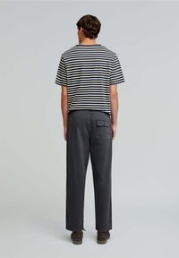 Cămașă cu mânecă scurtă, dungi în nuanțe de bleumarin și crem, asortată cu pantaloni largi, gri închis, care au un buzunar la spate și tivuri răsucite.