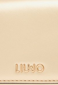 Portafoglio in pelle beige con una finitura testurizzata, caratterizzato da un logo metallizzato oro "LIU·JO" impresso sulla parte anteriore.