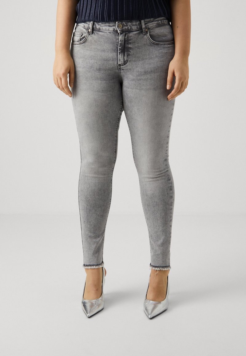 Vaqueros skinny grises con un lavado descolorido, diseño de cintura alta y dobladillos deshilachados, combinados con tacones plateados puntiagudos.