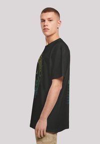 Černé bavlněné tričko s krátkým rukávem, s vícebarevným grafickým potiskem vepředu a po stranách, zdůrazňující uvolněný střih.