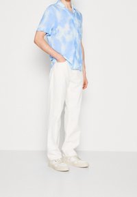 Kortärmad ljusblå tie-dye skjorta i kombination med vita byxor och beige sneakers. Slät tyg med avslappnad passform.