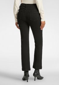 Jeans de mezclilla negra de pierna recta con una cintura de media altura, dos bolsillos traseros y un acabado limpio, combinados con botas negras de tobillo.