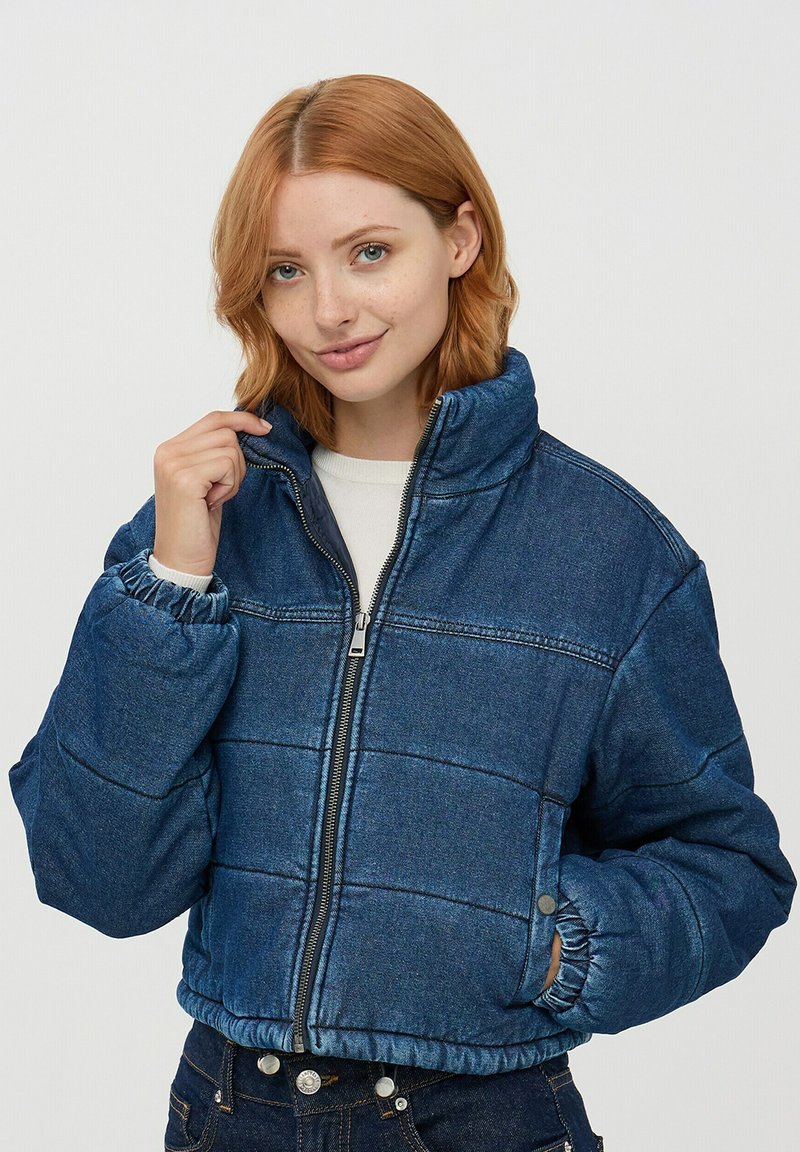 Niebieska puchowa kurtka z denimu z zamek błyskawicznym z przodu, wysokim kołnierzem, elastycznymi mankietami i elastycznym pasem; charakteryzuje się pikowanym wzorem przeszycia.