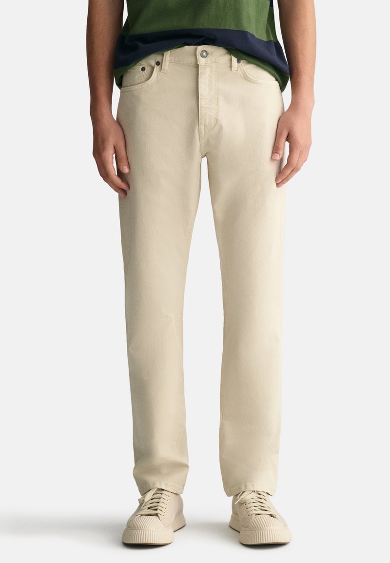 Beige bomullsbukser med rett snitt, fem lommer, metallbeslag og en lett glans. Båret med en grønn og marineblå stripete topp.