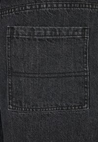 Närbild av en svart denim bakficka med synliga stygn och tygtextur.