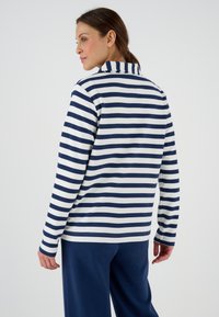 Maglietta a righe blu navy e bianca con maniche lunghe e colletto, realizzata in tessuto morbido, abbinata a pantaloni blu navy. Cuciture visibili lungo le maniche e l'orlo.