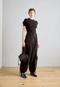 Camiseta negra de canalé, pantalones cargo de cintura alta con bolsillos, botas negras hasta el tobillo y un bolso negro redondo pequeño. Diseño simple y funcional.