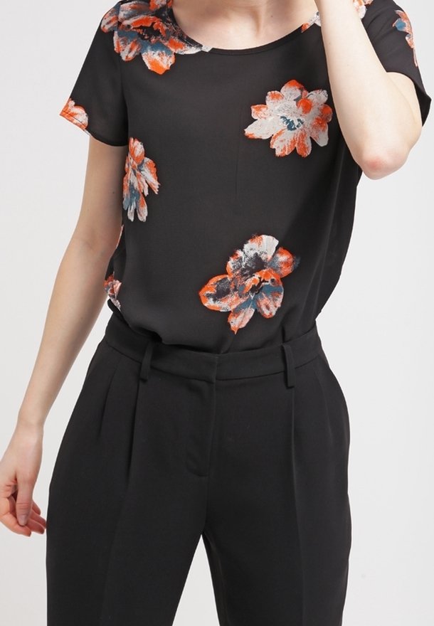 Blusa negra con flores de corte holgado, con patrones de flores naranjas y azules. Combinada con pantalones negros ajustados. Tejido suave.