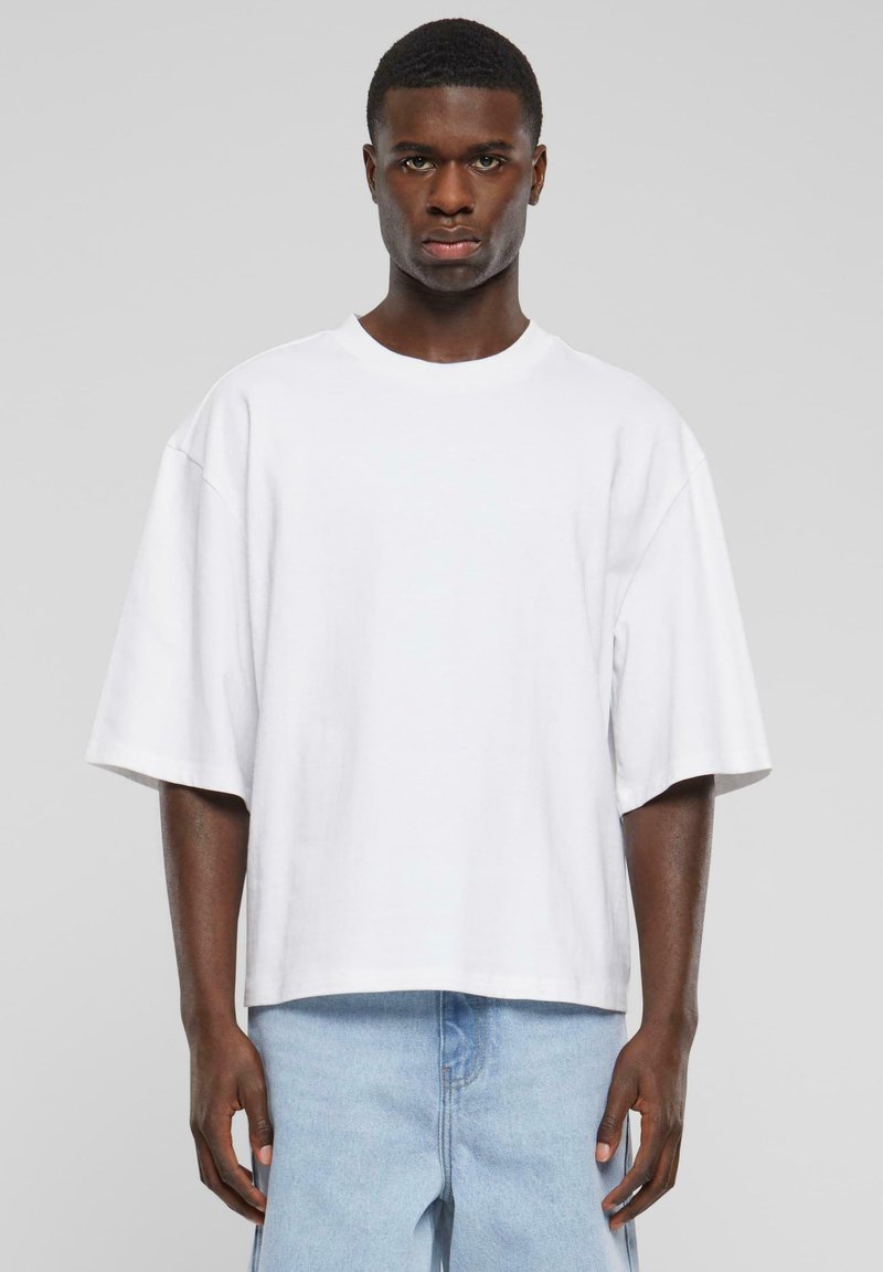 White oversized t-shirt made of cotton, featuring a round neckline and drop shoulder sleeves, paired with light blue denim jeans.