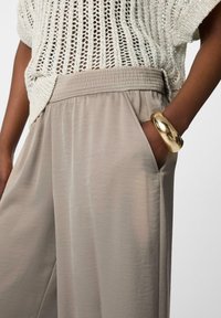 Beige, lichtgewicht broeken met een elastische tailleband en zijzakken, gedragen met een textuur, gebreide crème top en een metalen gouden armband.