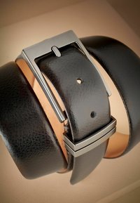 Ceinture en cuir noir avec une boucle rectangulaire en argent poli ; présente une texture lisse et plusieurs trous de réglage pour la taille.