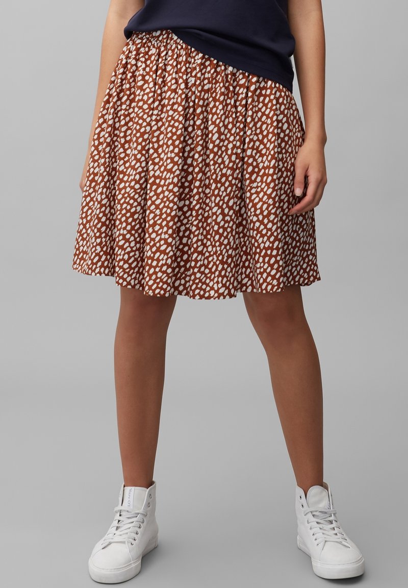 Gonna marrone con motivo a pois bianchi, design plissettato, vita arricciata, abbinata a sneaker alte bianche.