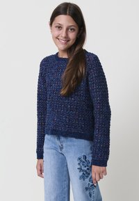 Maglione blu navy a maglia con un motivo texture, scollo rotondo e maniche lunghe, abbinato a jeans azzurri chiari con ricami floreali.